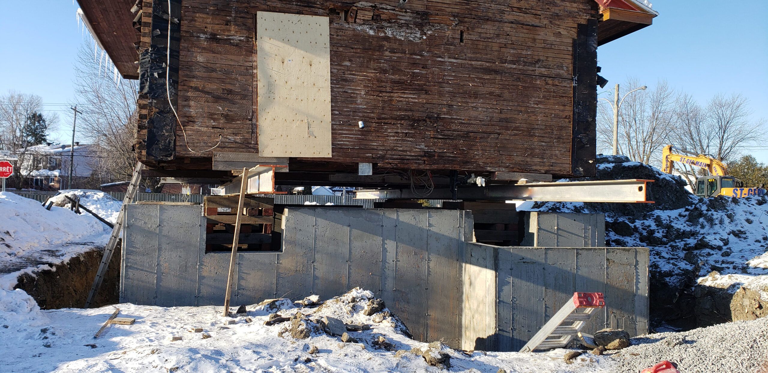 Foundation services in Quebec involving a house lifting project where the structure is elevated on steel beams to install a new concrete foundation, a method used for foundation repair or basement additions during winter conditions.