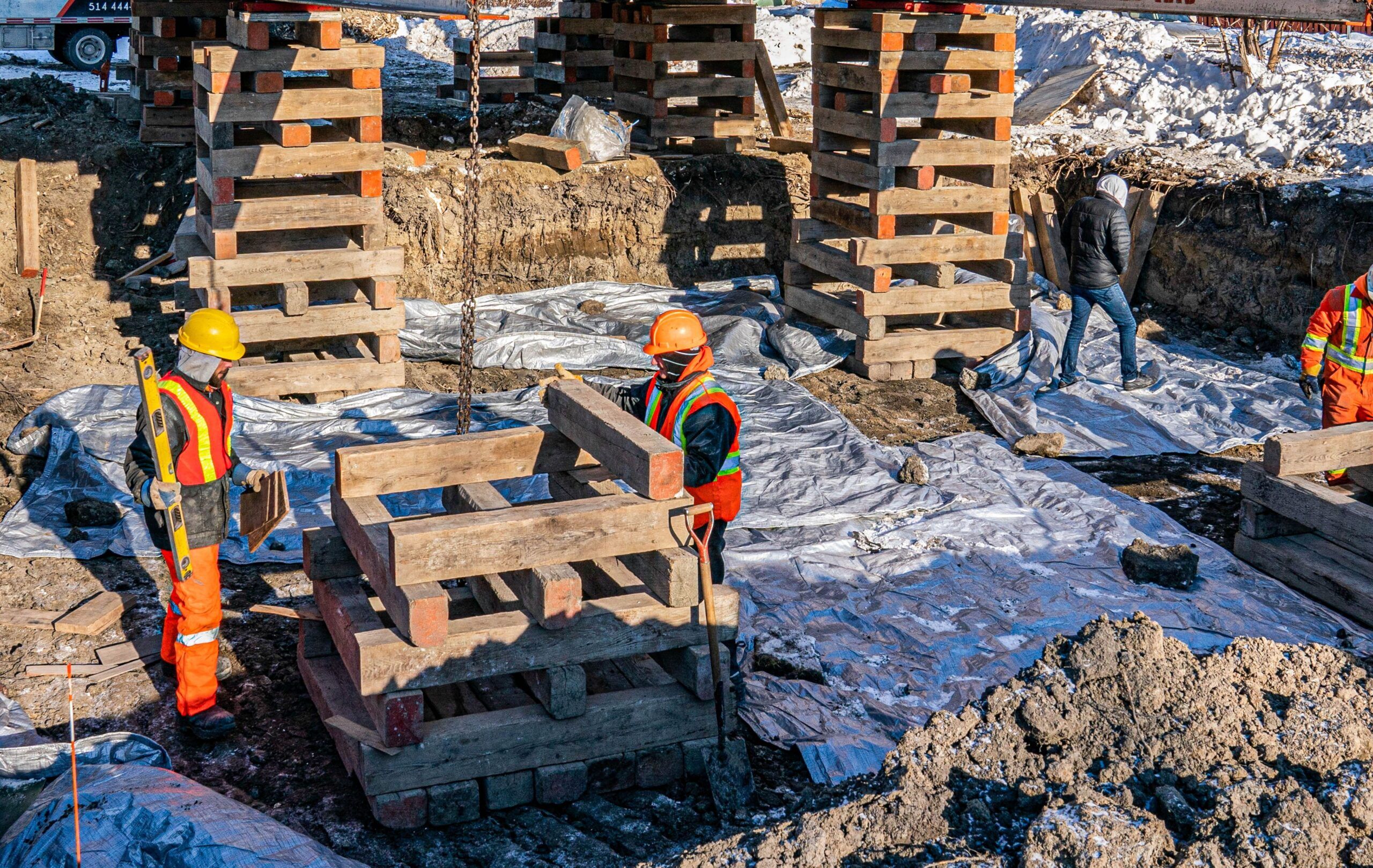 Lifting of Houses & Buildings Services in Quebec and Montreal shown at a construction site where workers reinforce a building foundation using wooden beams, pallets, and safety equipment.
