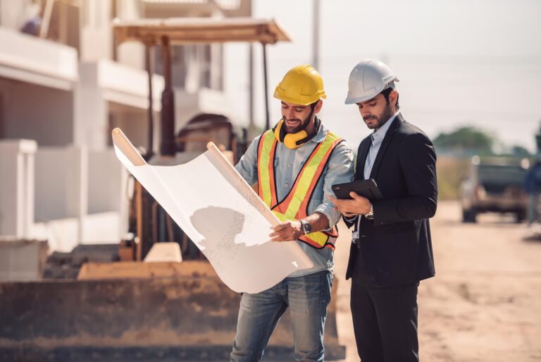 HMA Groupe Construction Membership Program – Two professionals, an architect and a construction engineer, reviewing blueprints on a construction site. The image represents collaboration, expertise, and the exclusive benefits of joining the HMA Groupe Construction Membership Program.